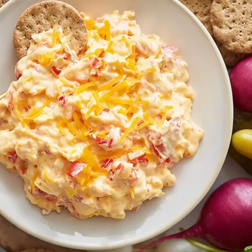 A bowl of rich, creamy pimento cheese spread, garnished with fresh chives.