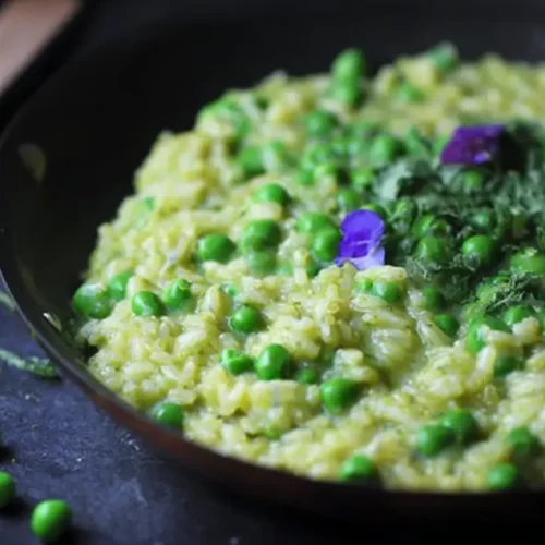 A vibrant bowl of spring pea risotto garnished with herbs.