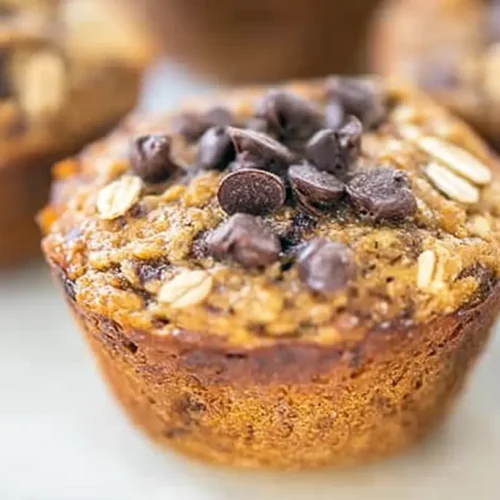 A close-up of freshly baked banana oatmeal muffins, golden brown and topped with oats.