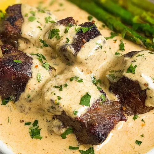 A close-up of garlic butter steak drizzled with parmesan cream sauce.