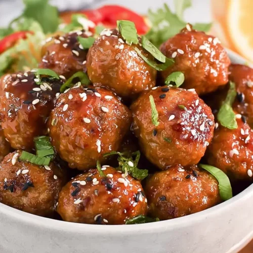 A close-up of slow cooker honey garlic meatballs in a glazed sauce, garnished with sesame seeds and green onions.