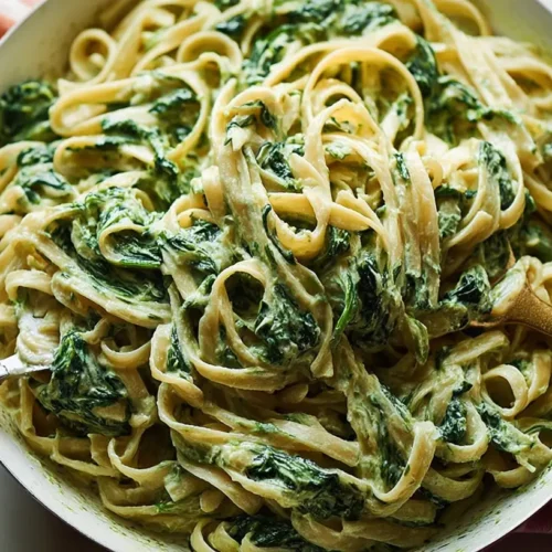 A dish of creamy spinach pasta garnished with fresh herbs.