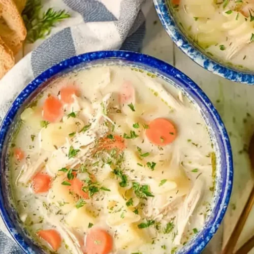 A bowl of crockpot creamy chicken soup garnished with fresh herbs and a drizzle of cream