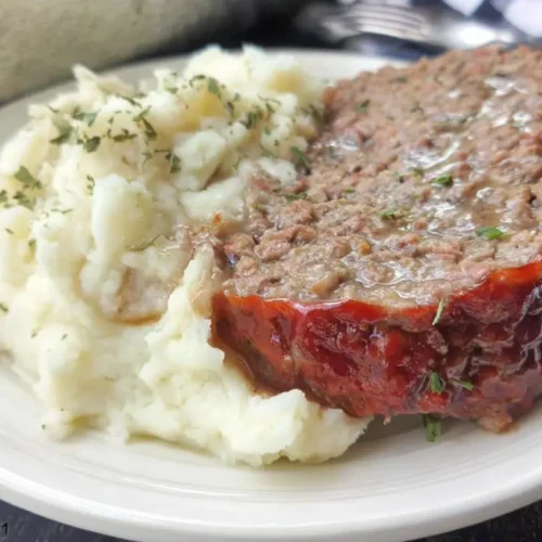 A hearty slice of meatloaf with a generous serving of mashed potatoes on a white plate.