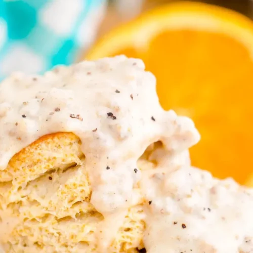 Fluffy biscuits drenched in creamy sausage gravy on a white plate