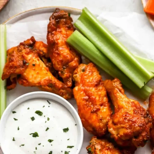 A plate piled high with crispy, saucy buffalo wings, ready to be eaten.