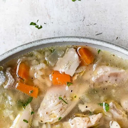 A steaming bowl of chicken and rice soup, garnished with fresh herbs.