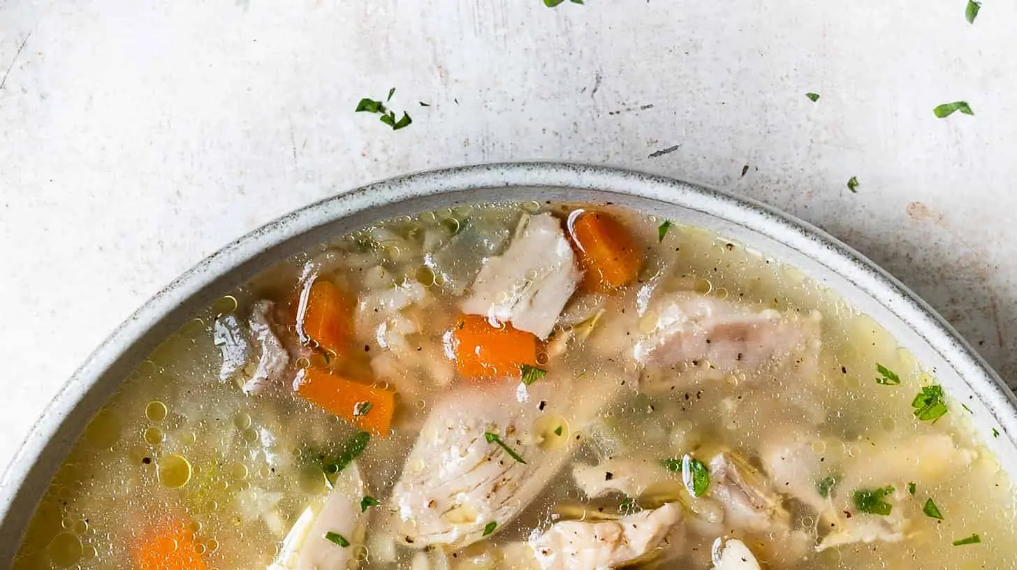 A steaming bowl of chicken and rice soup, garnished with fresh herbs.