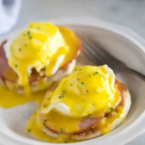 A close-up shot of perfectly poached eggs benedict with hollandaise sauce