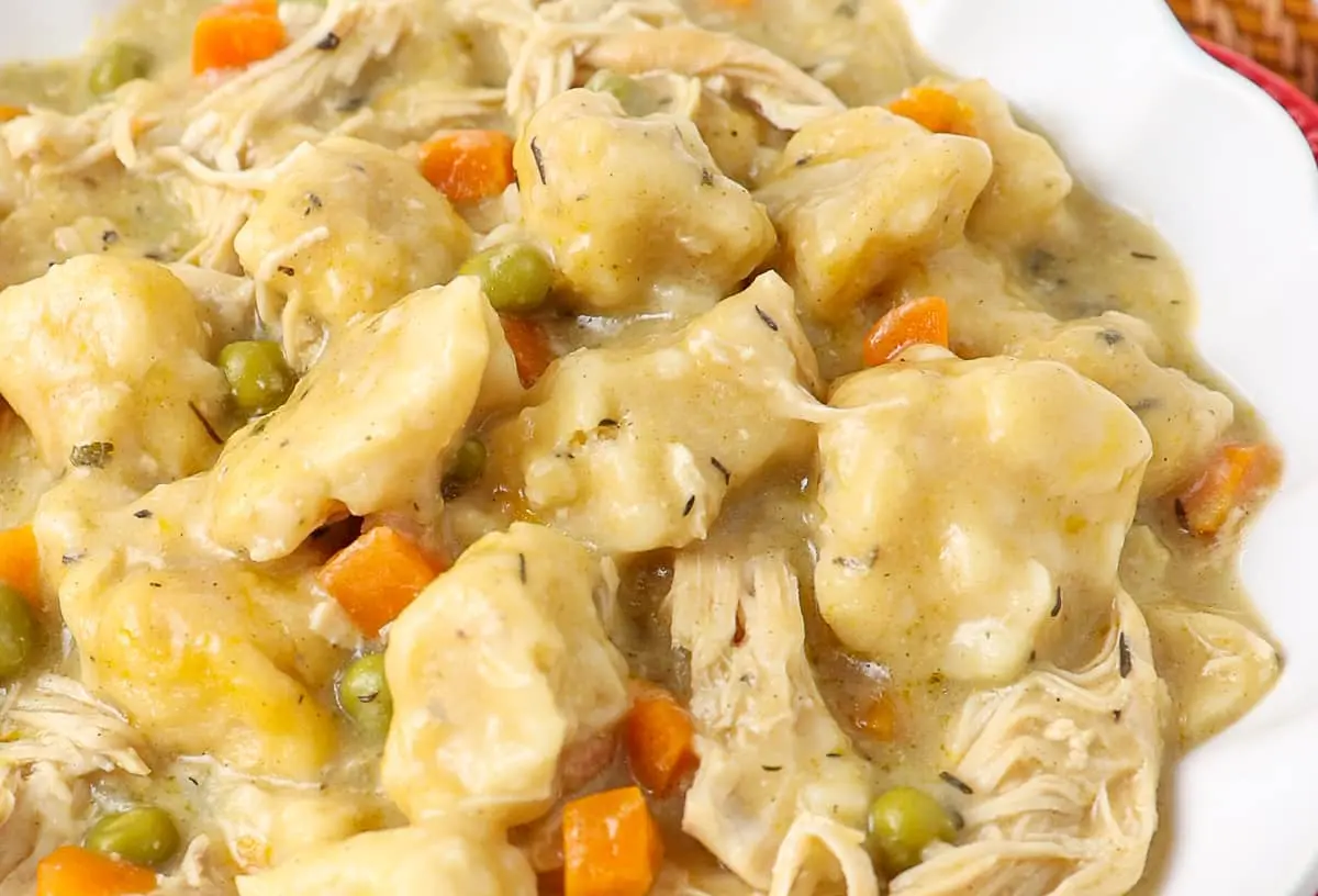 A steaming bowl of chicken and dumplings with herbs