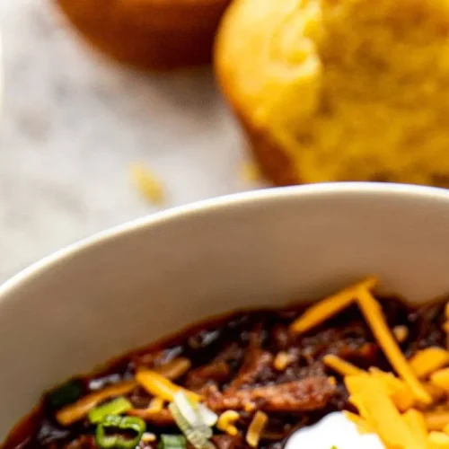A hot bowl of Texas style crockpot chili garnished with cheese and jalapeños.