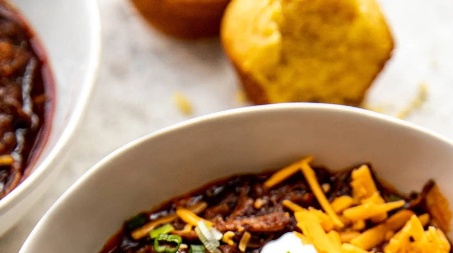 A hot bowl of Texas style crockpot chili garnished with cheese and jalapeños.